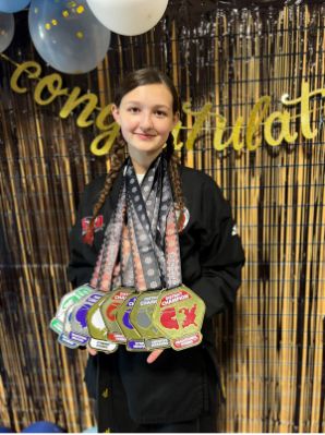 mb-3 Persona vestida con un uniforme de artes marciales sosteniendo varias medallas de campeonato con un fondo de felicitación y globos.