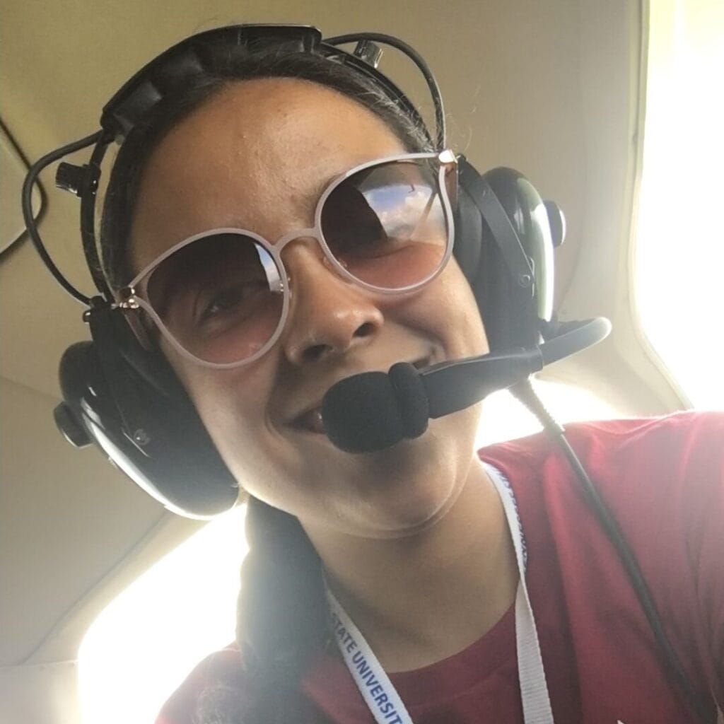 Persona con gafas de sol de aviador y auriculares con micrófono, sonriendo en el interior de un avión.