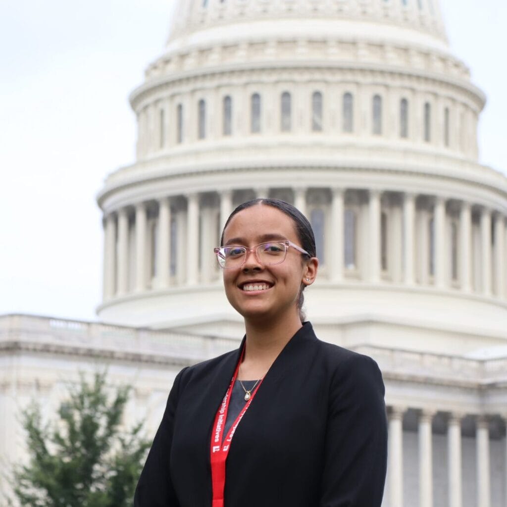 Un individuo vestido con americana negra y gafas, sonriente, frente al edificio del Capitolio de los Estados Unidos.
