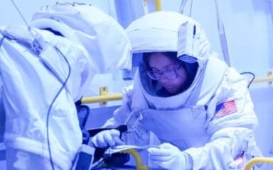Dos astronautas con trajes espaciales trabajan con equipos en una instalación de entrenamiento.