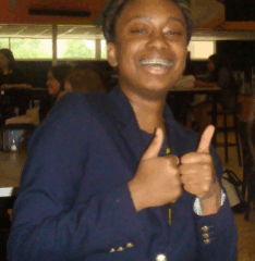 Persona con una chaqueta azul marino haciendo un gesto de aprobación con los pulgares en una cafetería interior.