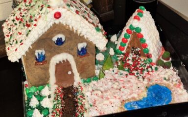 Una casita de jengibre decorada, presentada en una bandeja con glaseado, detalles de caramelo y una temática navideña nevada.