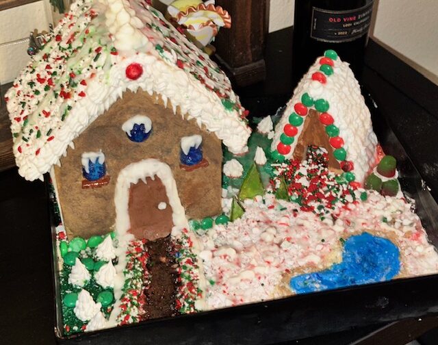 Una casita de jengibre decorada, presentada en una bandeja con glaseado, detalles de caramelo y una temática navideña nevada.