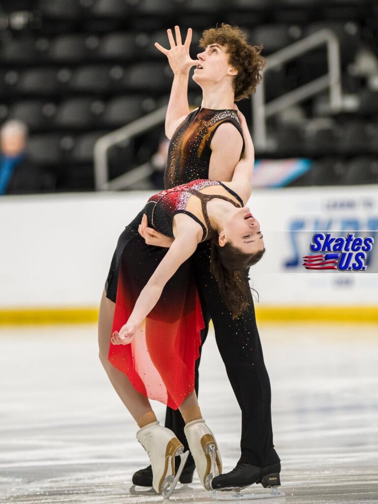 Jane Calhoun realiza un espectacular movimiento de danza sobre hielo junto a su pareja durante una competición de patinaje artístico.